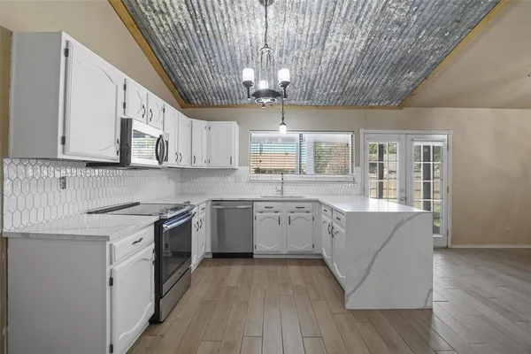 a large kitchen with granite countertop a stove top oven a sink dishwasher and white cabinets with wooden floor