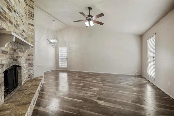 an empty room with wooden floor fireplace and windows