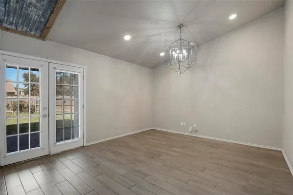an empty room with wooden floor chandelier and windows