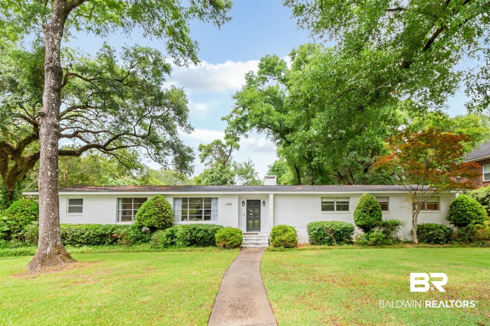 4596 Hawthorne Place Mobile, AL 36608 - Photo 1 of 34 Single-story residence featuring a white brick exterior, a dark entry door with sidelights, and multiple large windows