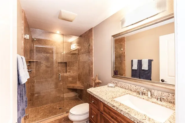 a bathroom with a granite countertop sink toilet mirror and shower