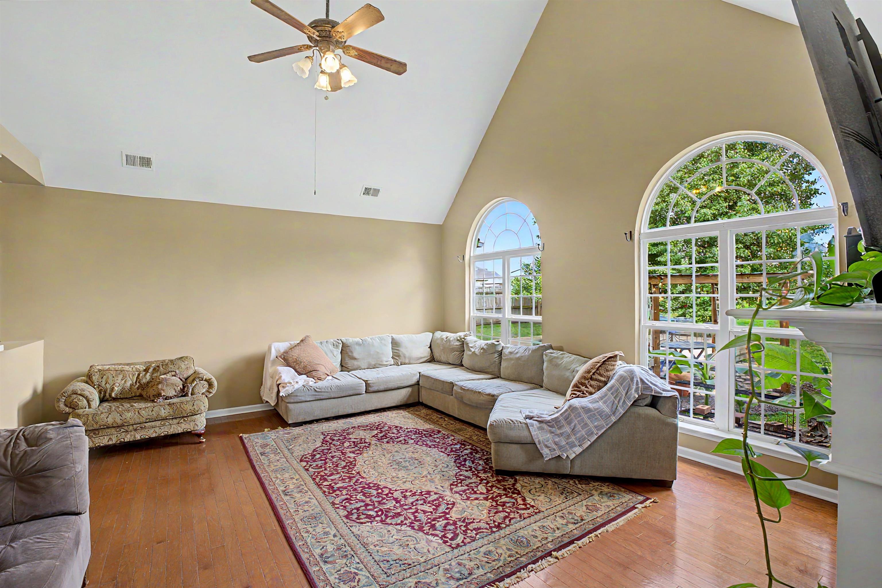 134 Rembert Drive Atoka, TN 38004 - Photo 10 of 38 Vaulted ceiling living room featuring arched windows, wood-finish flooring, and a ceiling fan with integrated lighting
