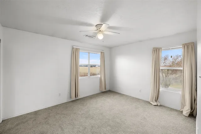 an empty room with chandelier fan and windows