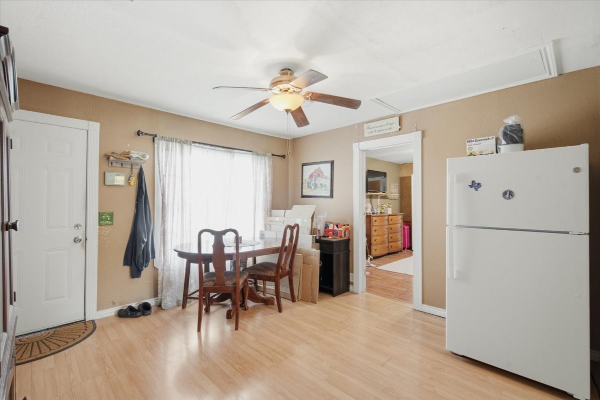 765 Norcross Road Wallis, TX 77485 - Photo 11 of 42 This cozy dining area features laminate wood flooring, a ceiling fan, It has a large window for natural light, a white refrigerator, and access to another room through an open doorway.