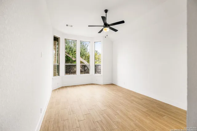 a view of empty room with wooden floor and fan