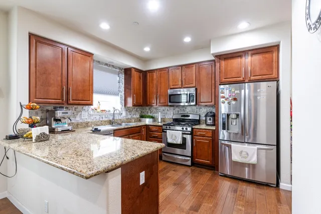 a kitchen with stainless steel appliances granite countertop a refrigerator a stove top oven a sink and dishwasher with wooden floor