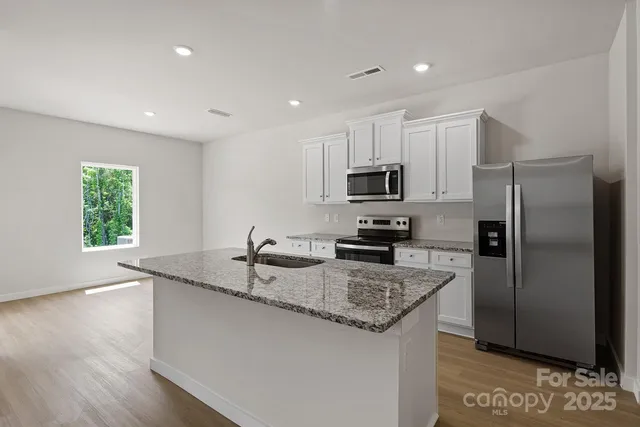 a kitchen with granite countertop a sink a center island stainless steel appliances and a window