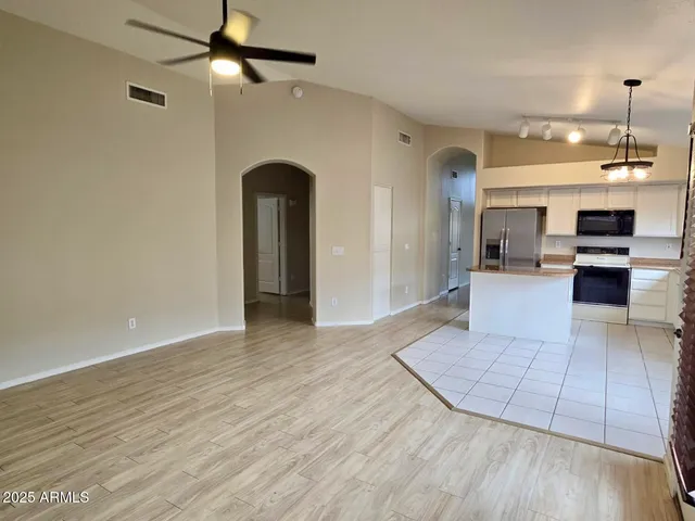 an empty room with wooden floor a ceiling fan a kitchen view and a fireplace
