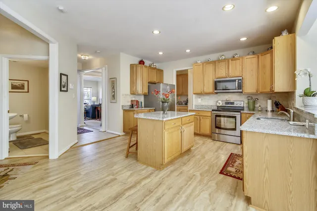 a kitchen with stainless steel appliances granite countertop a stove top oven a sink a refrigerator and white cabinets with wooden floor