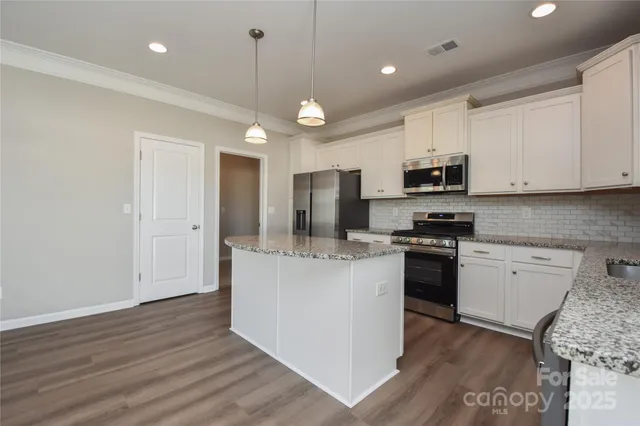 a kitchen with stainless steel appliances granite countertop a refrigerator a stove top oven a sink and dishwasher with wooden floor