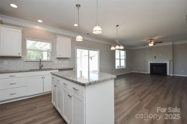 a kitchen with granite countertop a stove a sink and white cabinets with wooden floor