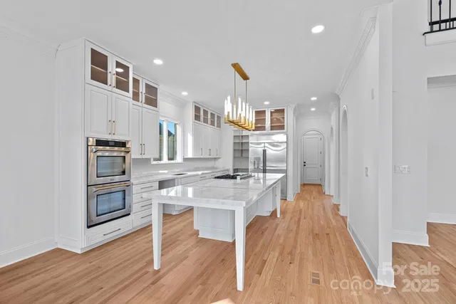 a kitchen with stainless steel appliances granite countertop a refrigerator oven a sink dishwasher and white cabinets with wooden floor