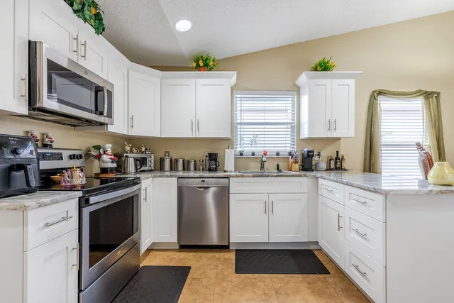 a kitchen with granite countertop white cabinets stainless steel appliances a sink and a window