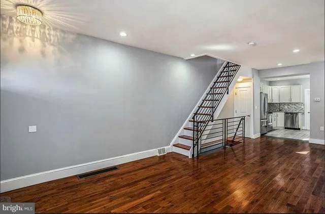 a view of an empty room with wooden floor stairs and a way to kitchen