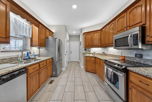 a kitchen with stainless steel appliances granite countertop a stove top oven a sink dishwasher a refrigerator and a microwave oven with wooden cabinets