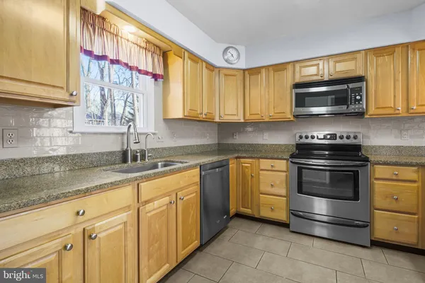 a kitchen with stainless steel appliances granite countertop a sink a stove a refrigerator cabinets and a window