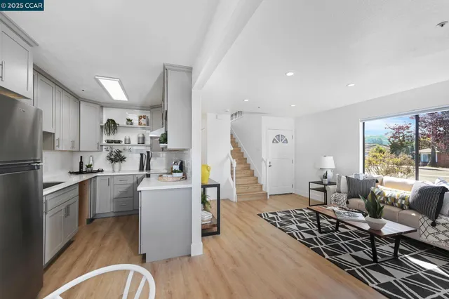 a living room with stainless steel appliances a dining table wooden floor and a large window