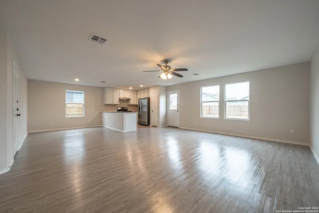 a view of an empty room and a kitchen with wooden floor