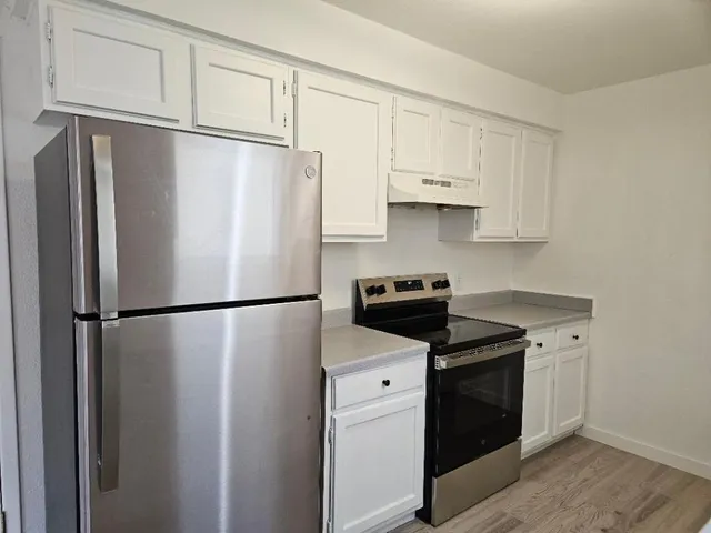 a white refrigerator freezer and a stove sitting inside of a kitchen with stainless steel appliances wooden floor