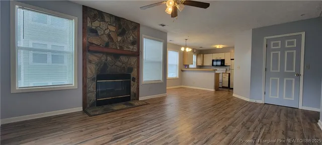an empty room with wooden floor kitchen view and windows