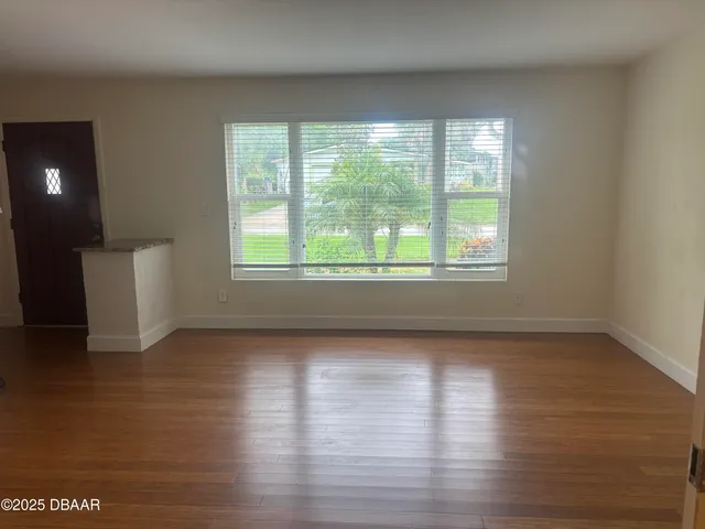 a view of an empty room with wooden floor and a window