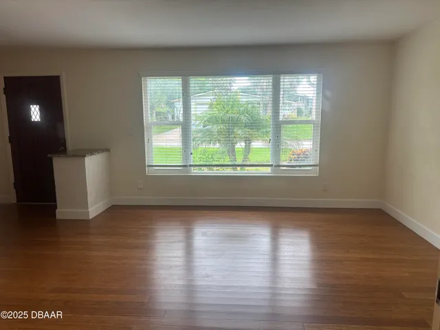 a view of an empty room with wooden floor and a window