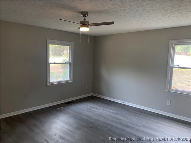 an empty room with wooden floor fan and windows