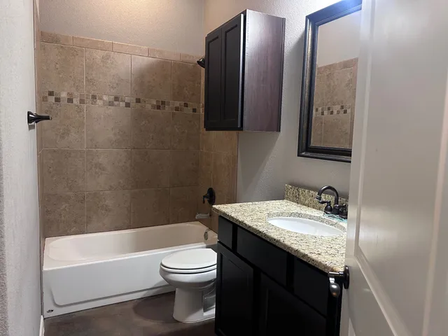 a bathroom with a granite countertop bathtub sink vanity mirror and toilet