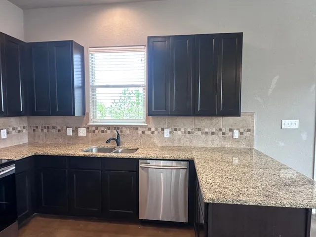 a kitchen with granite countertop a sink window and cabinets