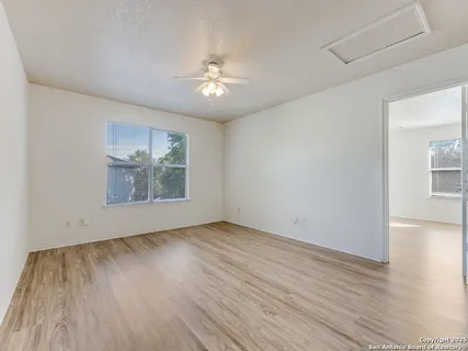 an empty room with wooden floor chandelier fan and windows