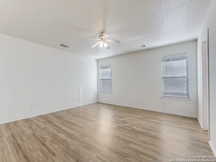 an empty room with wooden floor ceiling fan and windows