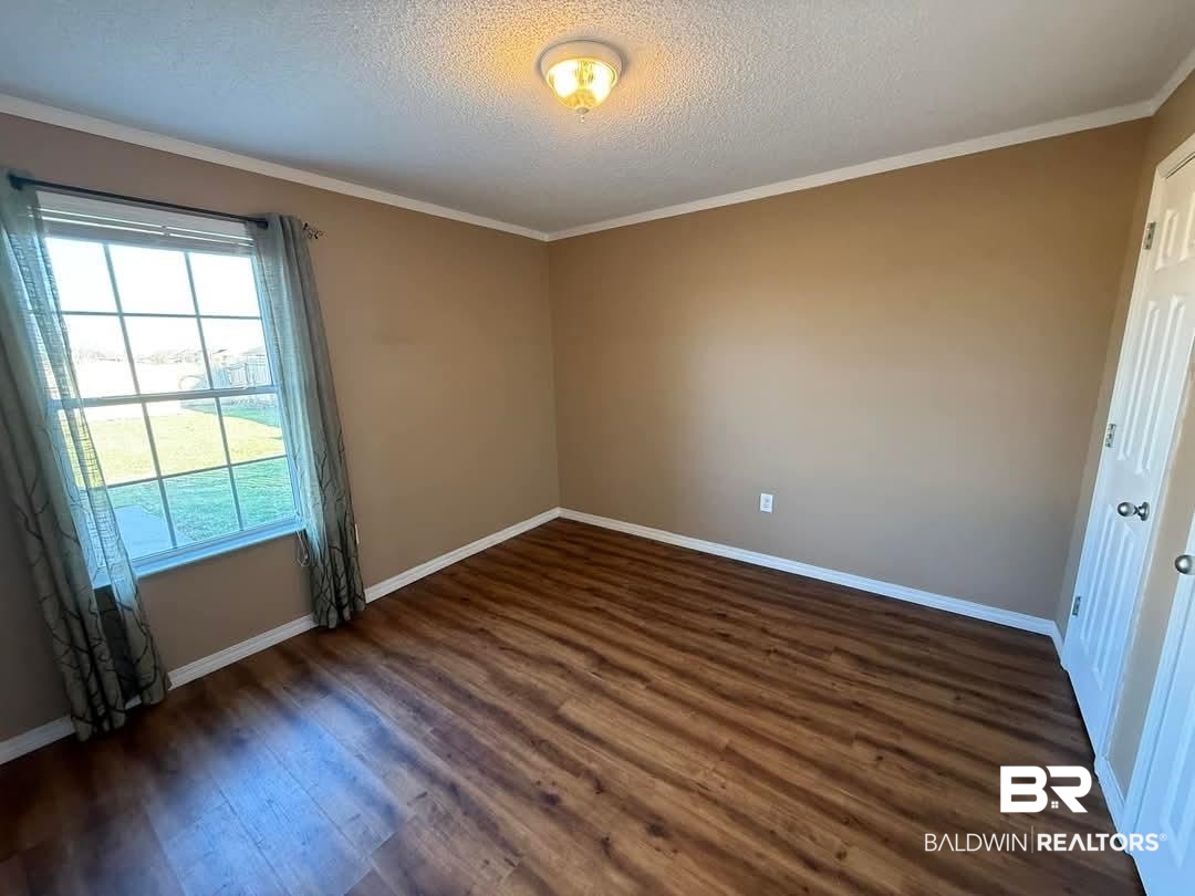 8912 Sherman Road Foley, AL 36535 - Photo 20 of 35 Spare room featuring dark wood-style floors, ornamental molding, a textured ceiling, and baseboards