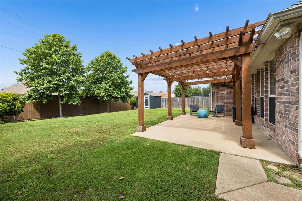 9217 Inverness Drive Rowlett, TX 75089 - Photo 27 of 40 Pergola-Covered Patio — The backyard patio is framed by a wood pergola and string lights, creating an inviting spot to unwind, dine outdoors, or enjoy the evening breeze.