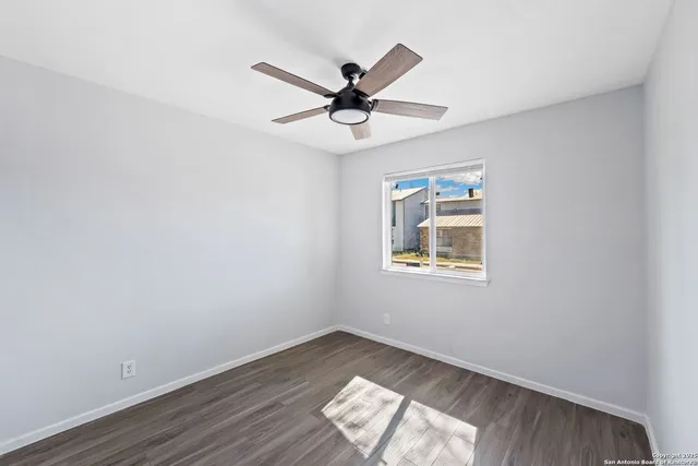 an empty room with wooden floor a ceiling fan and windows