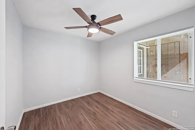 an empty room with wooden floor ceiling fan and windows