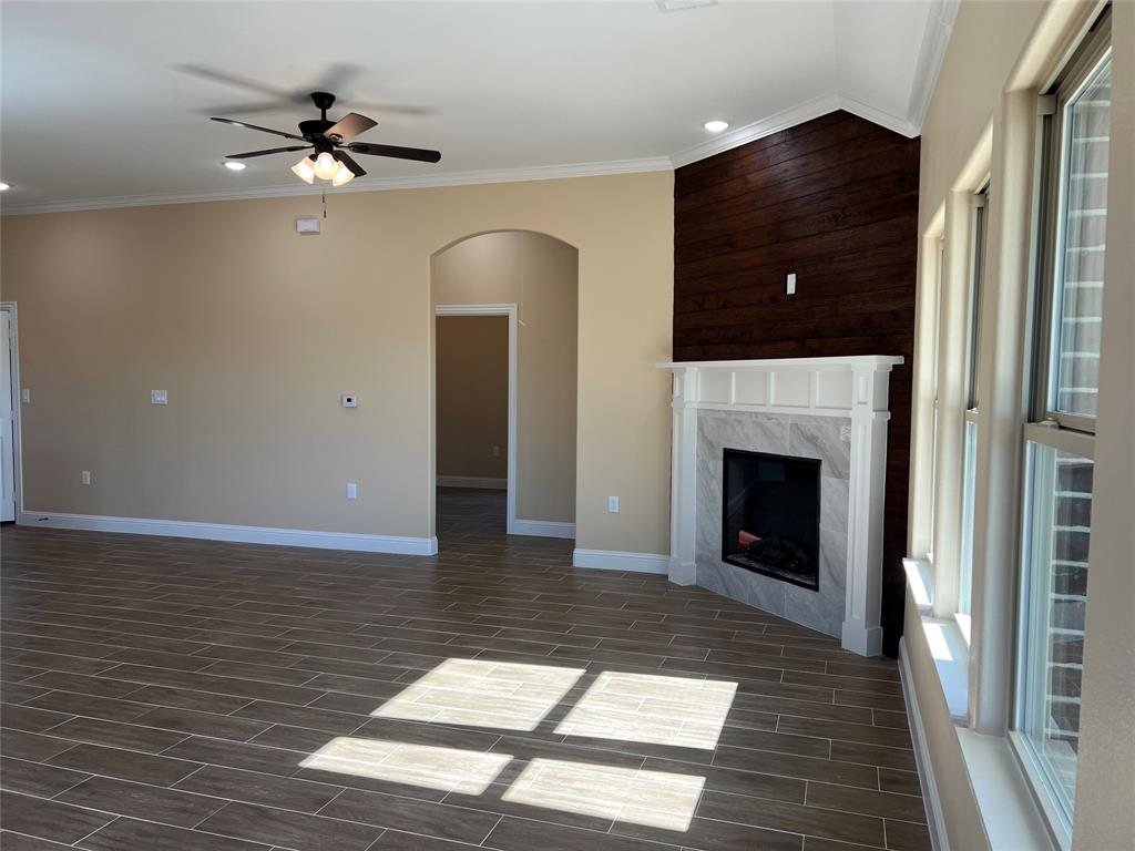 7363 Northeast County Road Rice, TX 75155 - Photo 3 of 4 Spacious living area featuring wood-finish tile flooring, a corner fireplace with a white mantel and stone surround, and an accent wall with horizontal wood paneling
