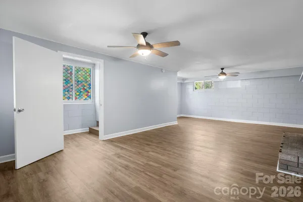 a view of an empty room with wooden floor and a ceiling fan