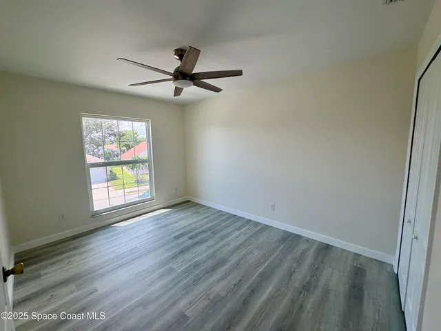 an empty room with wooden floor fan and windows
