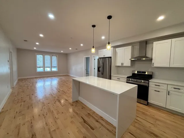 a large kitchen with granite countertop a stove a sink a refrigerator and white cabinets with wooden floor