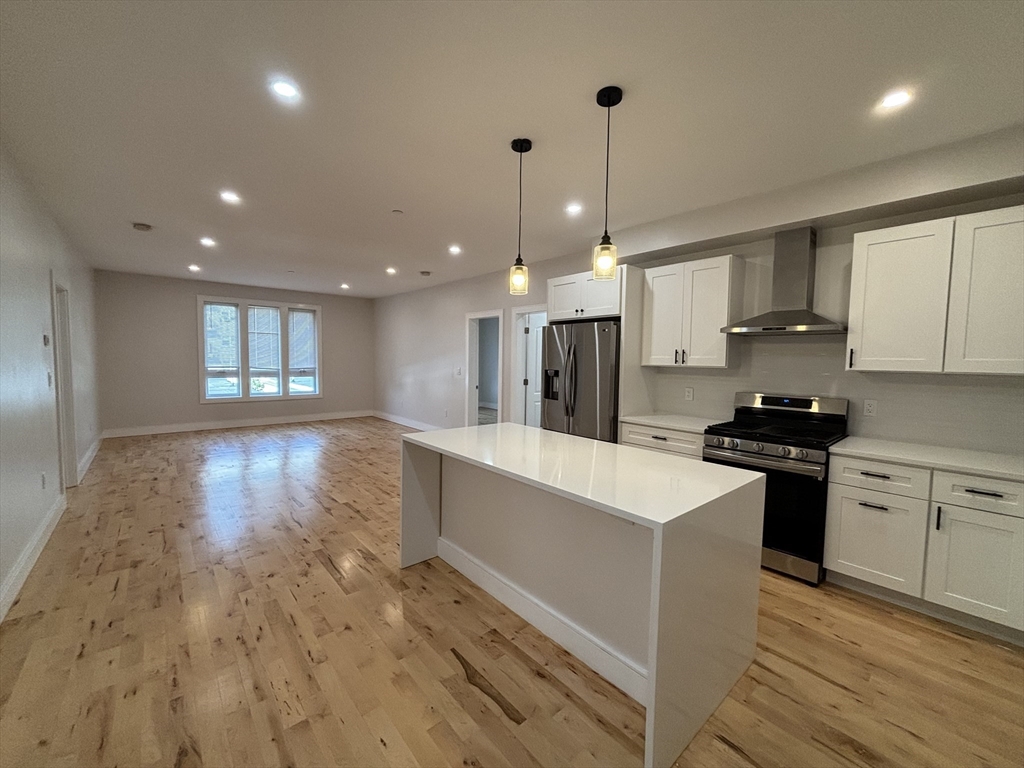 a large kitchen with granite countertop a stove a sink a refrigerator and white cabinets with wooden floor