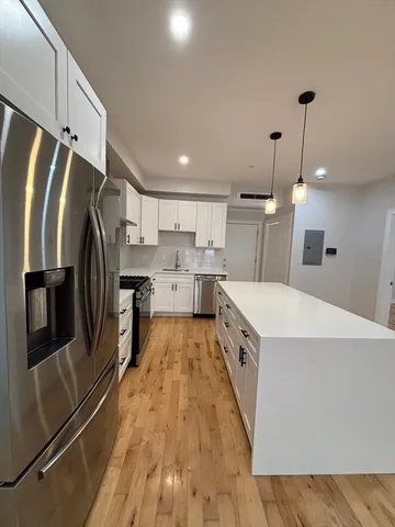 a large kitchen with stainless steel appliances kitchen island a stove a refrigerator a oven and a sink with wooden floor