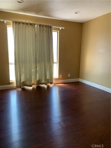 an empty room with wooden floor and windows with curtains