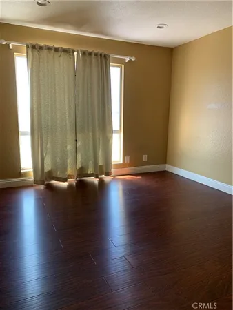 an empty room with wooden floor and windows with curtains