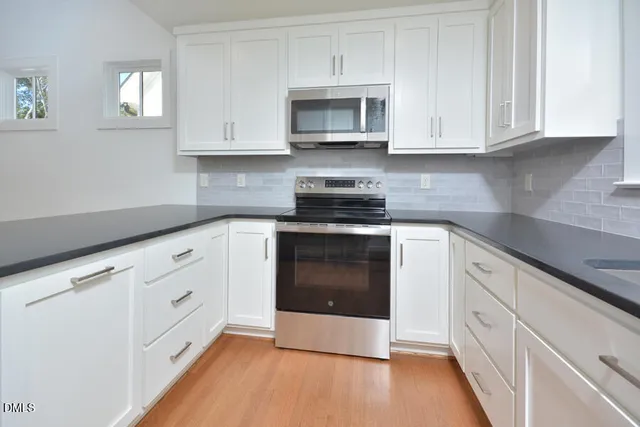 a kitchen with stainless steel appliances granite countertop white cabinets granite counter tops and a wooden floor