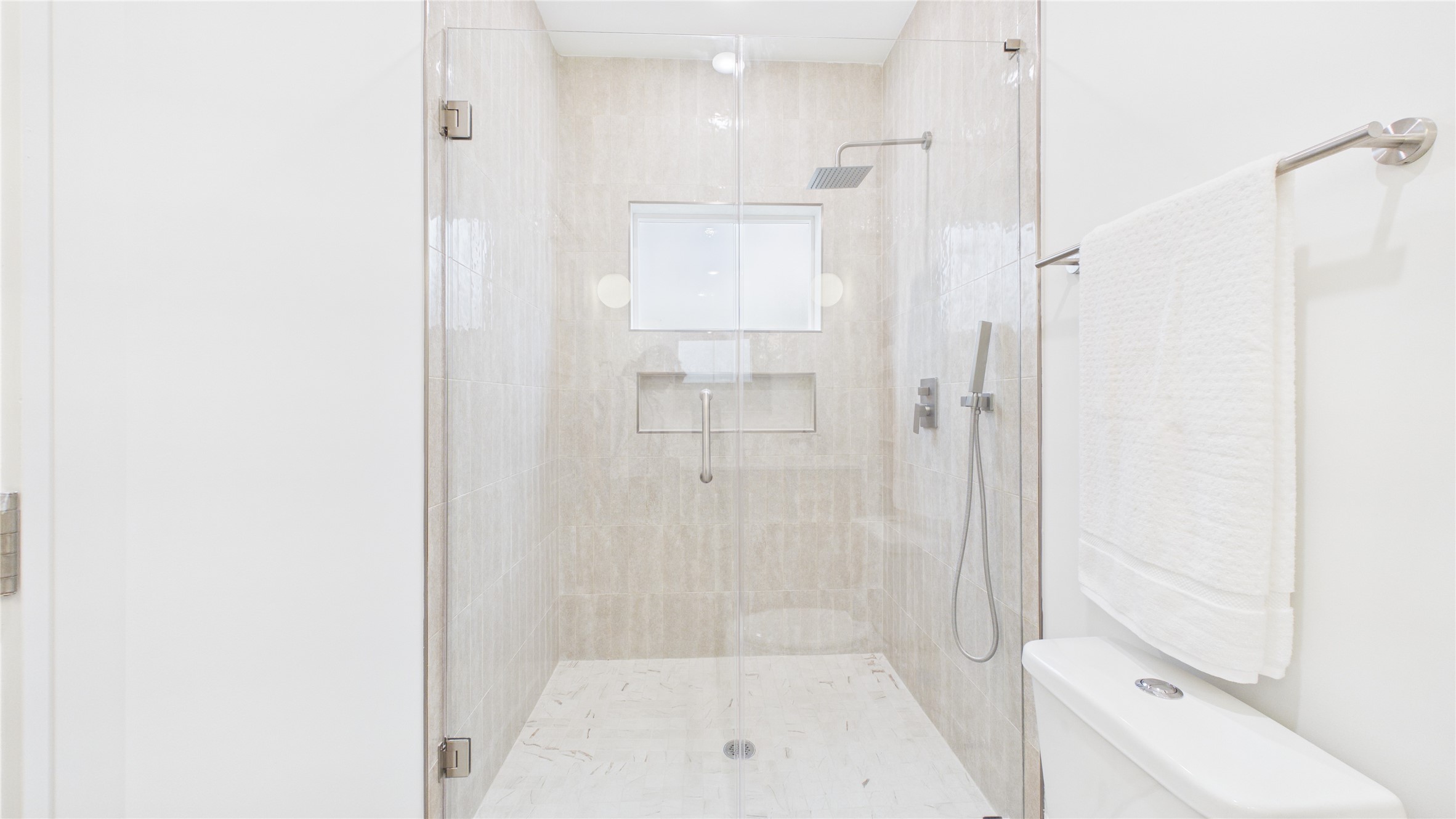 602 Skyland Terrace Way Houston, TX 77009 - Photo 10 of 40 This is a modern, sleek bathroom with a walk-in glass shower featuring a rainfall showerhead. It has light beige tiles, a built-in shelf, and a clean, minimalist design. The white walls and fixtures add to the bright, spacious feel.