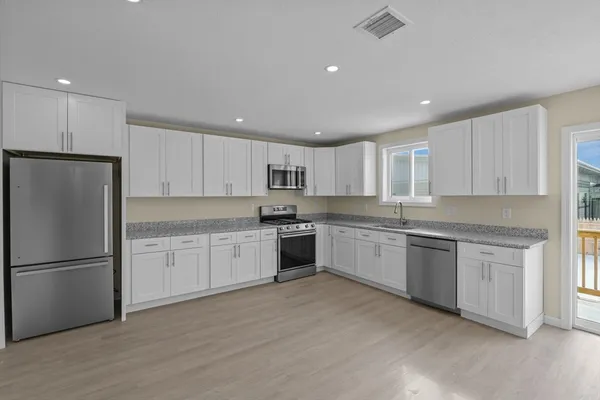 a large kitchen with granite countertop a refrigerator oven a sink dishwasher white cabinets and a granite countertops with wooden floor