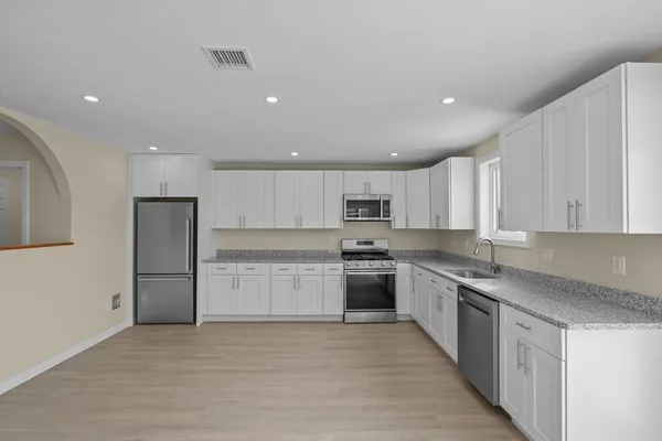 a large kitchen with stainless steel appliances granite countertop a stove a sink a refrigerator and white cabinets with wooden floor