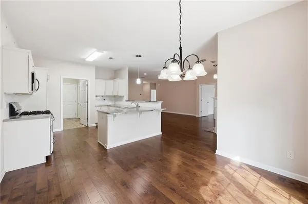 a kitchen with kitchen island granite countertop a stove top oven a sink dishwasher a refrigerator and white cabinets with wooden floor