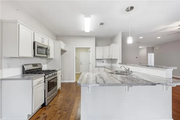 a large white kitchen with stainless steel appliances granite countertop a stove and a wooden floors