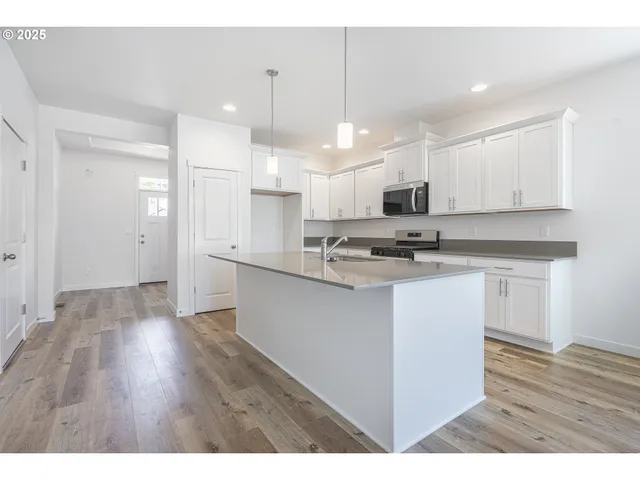 a kitchen with stainless steel appliances kitchen island granite countertop a sink a stove a refrigerator and white cabinets